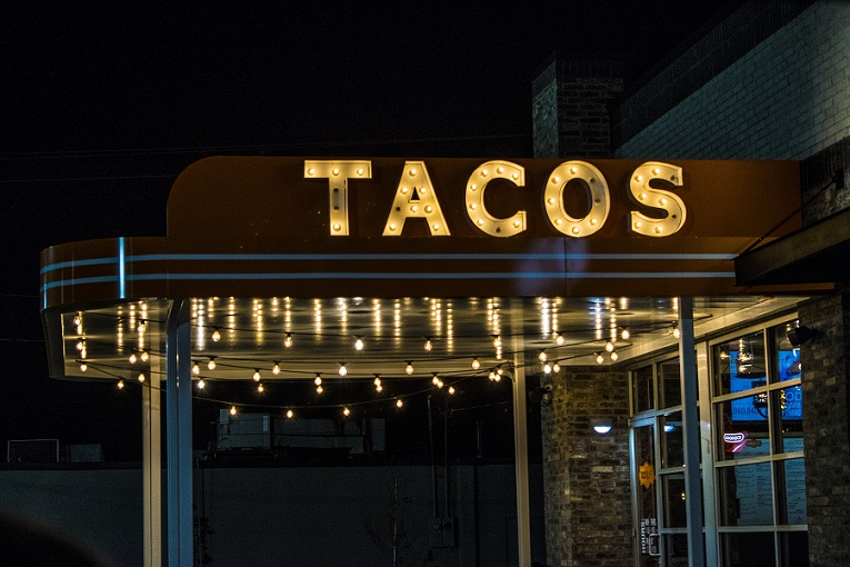 A restaurant sign for Tacos lit up at night